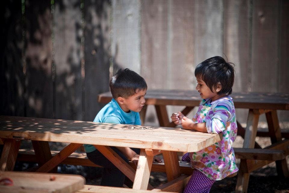 Two children sitting at a picnic table looking at each other