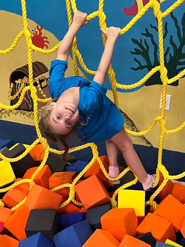 Child hanging upside down on a yellow rope net over foam blocks