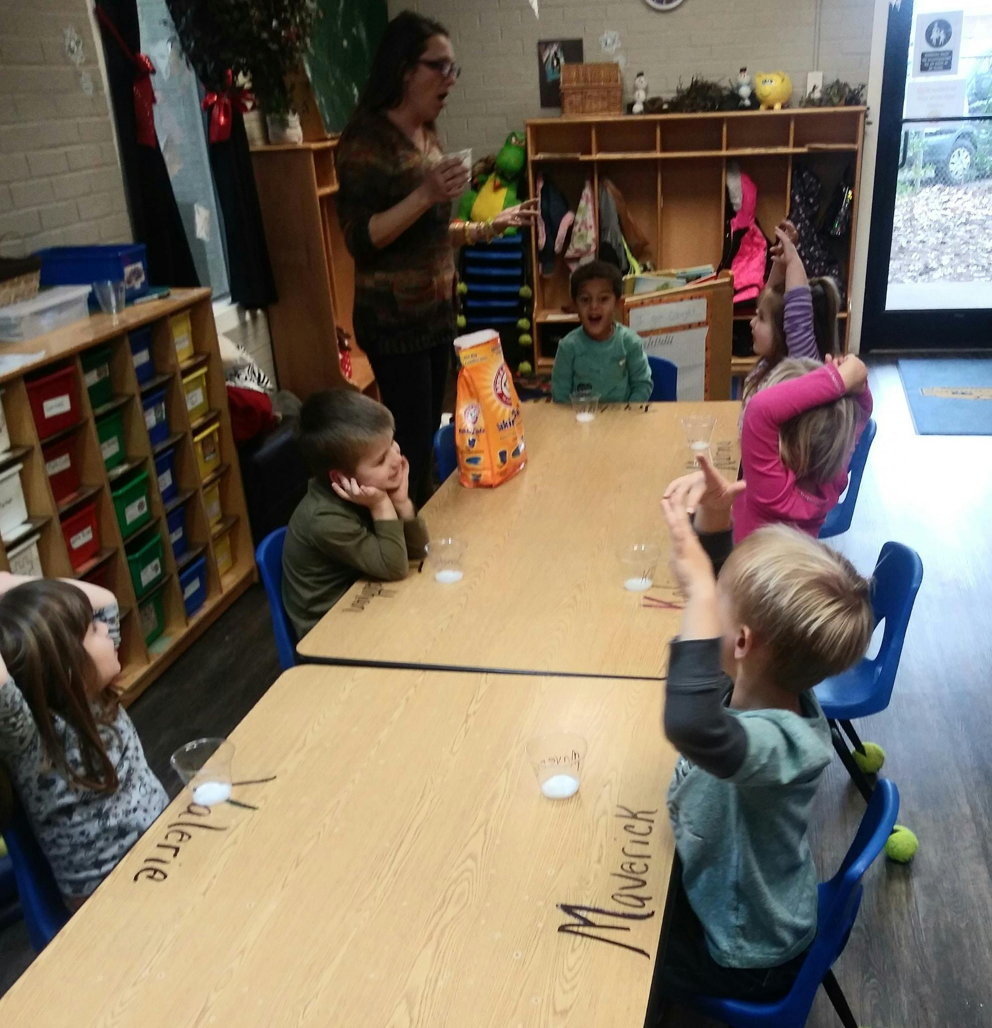Adult speaking to children seated at tables in a classroom
