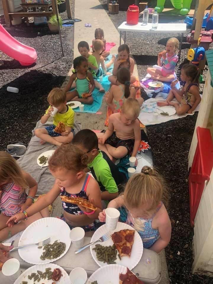 Children sitting on blankets eating pizza and green beans outdoors