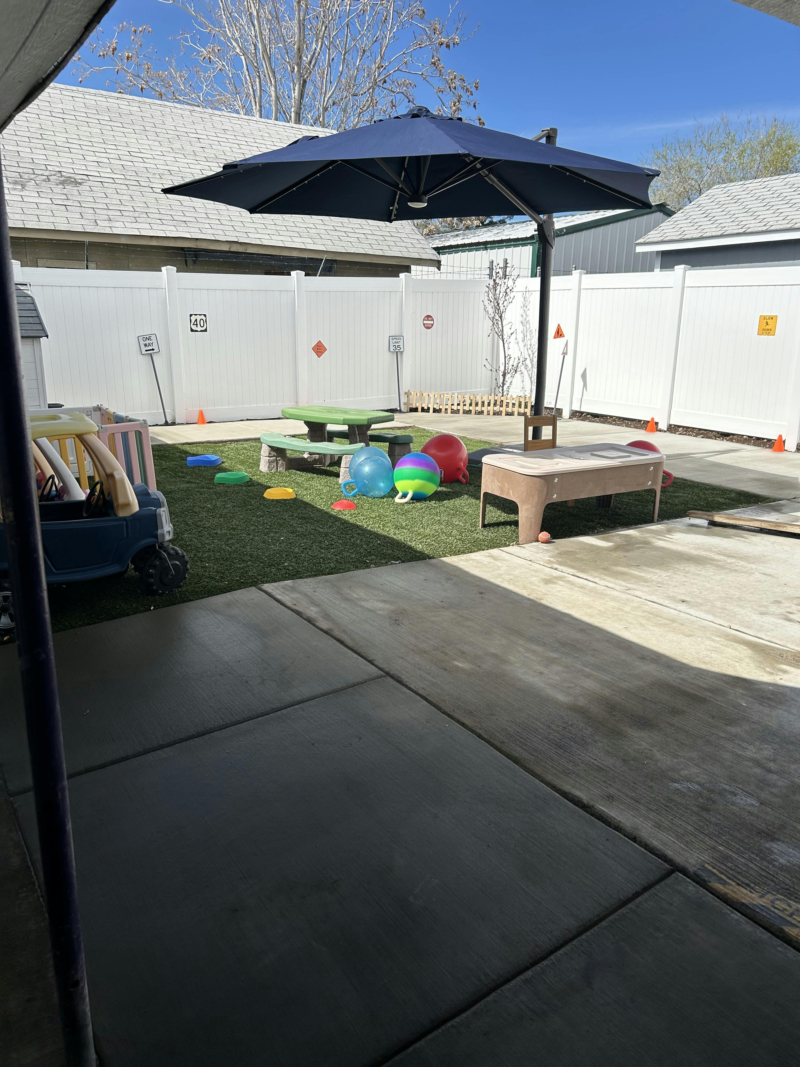 Childcare backyard with artificial turf, umbrella, picnic table, and toys
