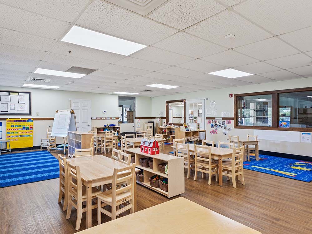 Empty classroom with small wooden tables and chairs, and play mats