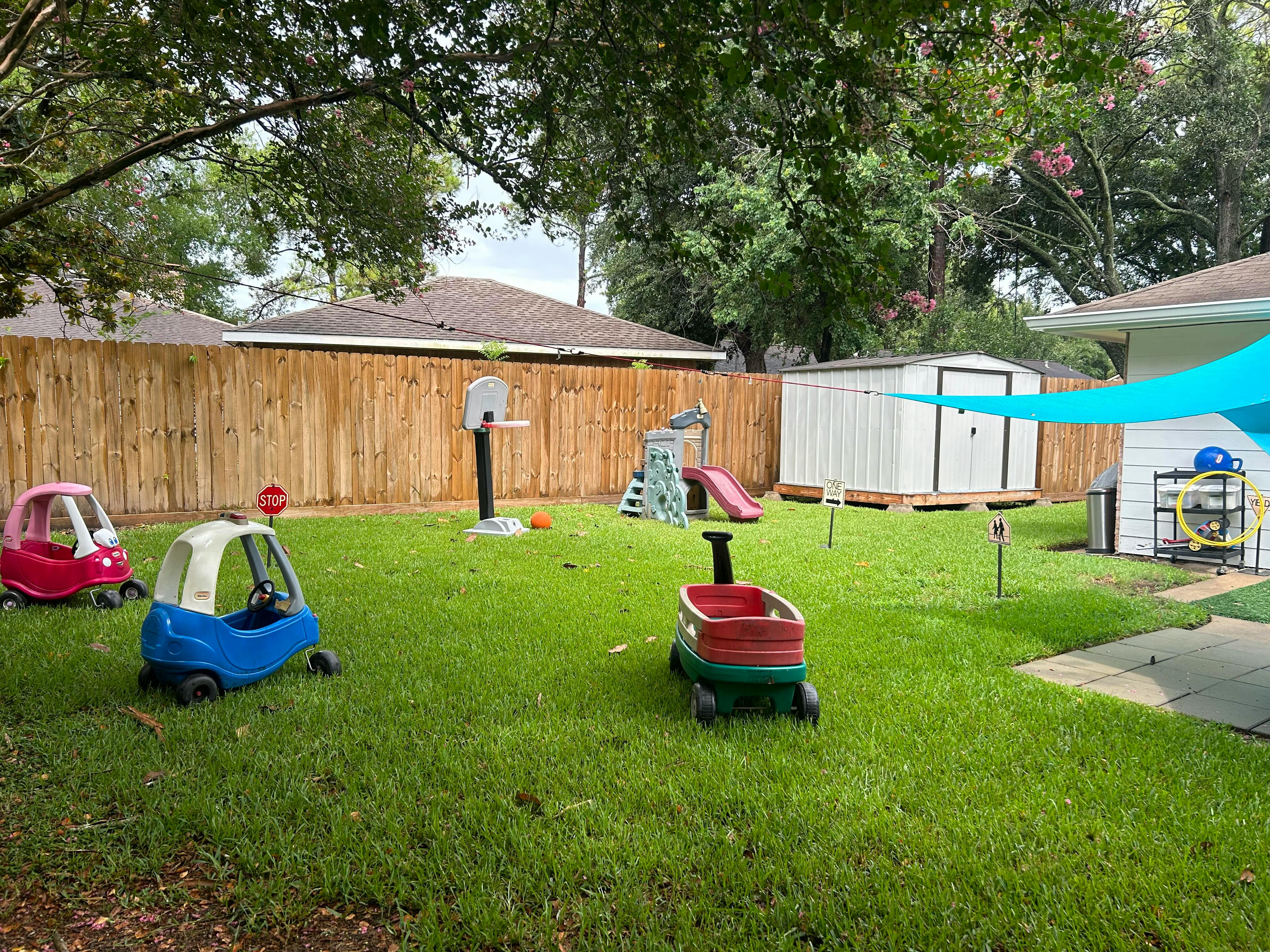 Backyard with children's play equipment including toy cars, wagon, basketball hoop, and slide