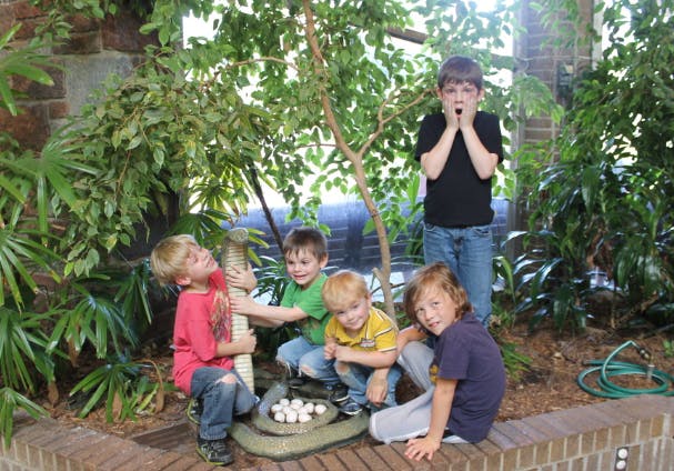 Five children interacting with a snake statue and eggs