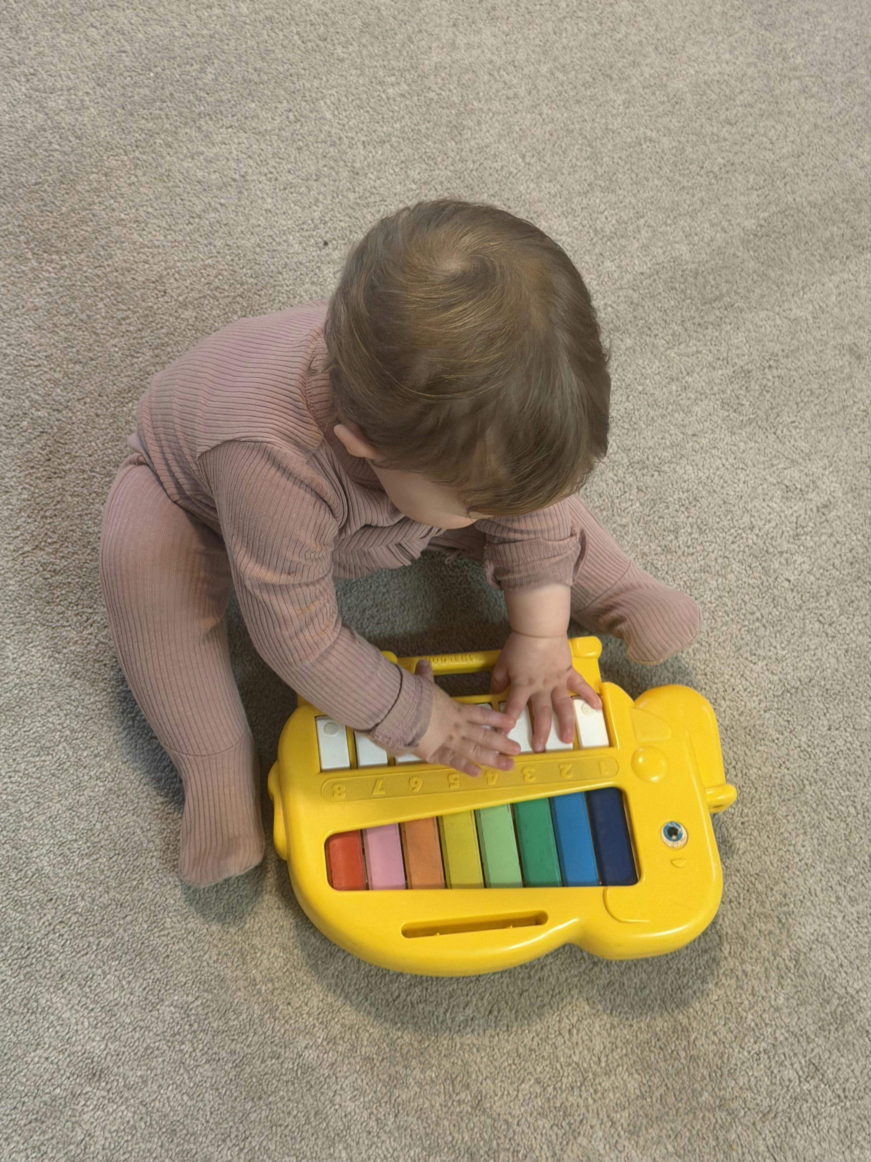 Child playing with a yellow toy piano with colorful keys