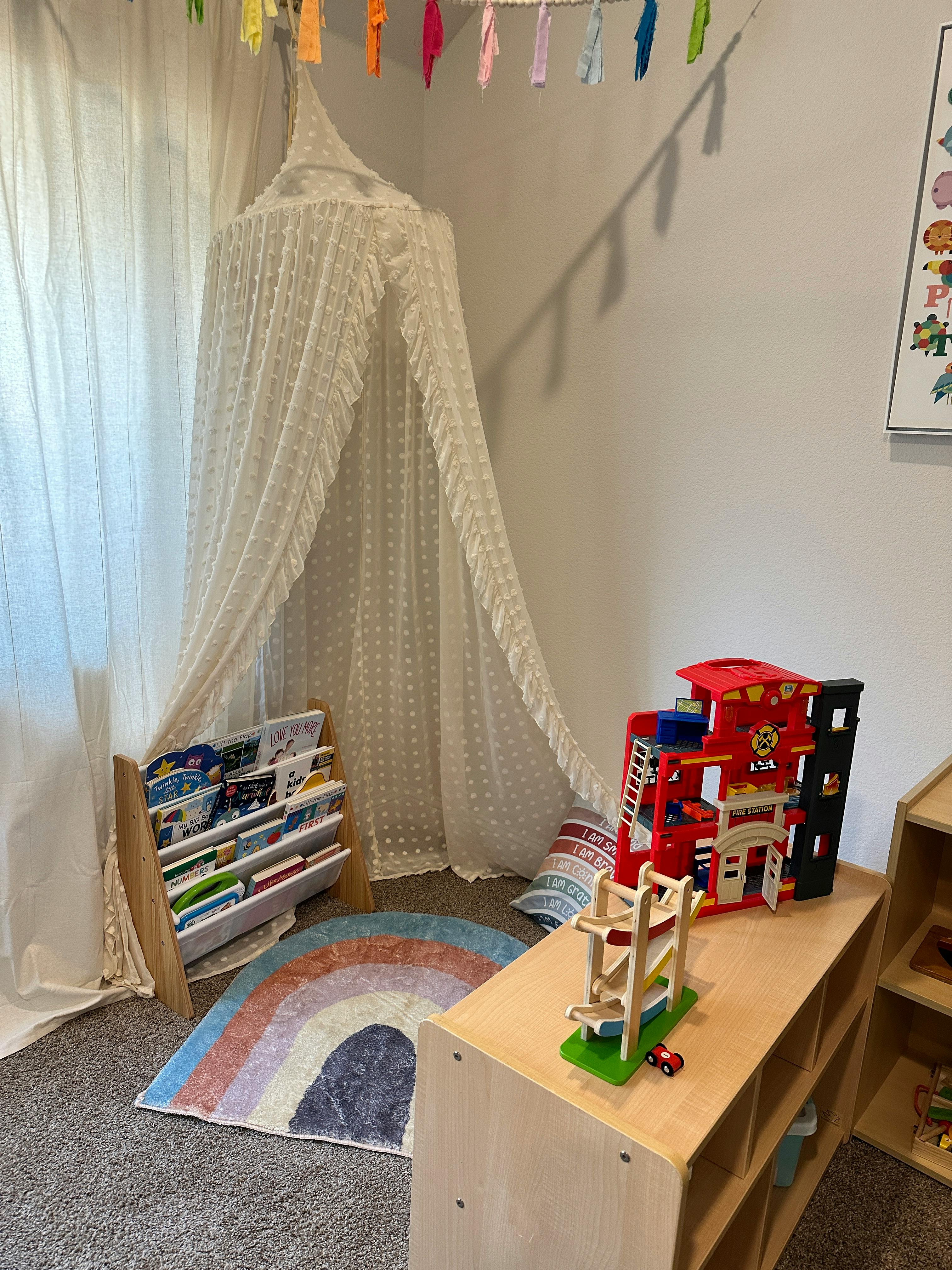 Children's play area with a canopy, bookshelf, rainbow rug, and toys
