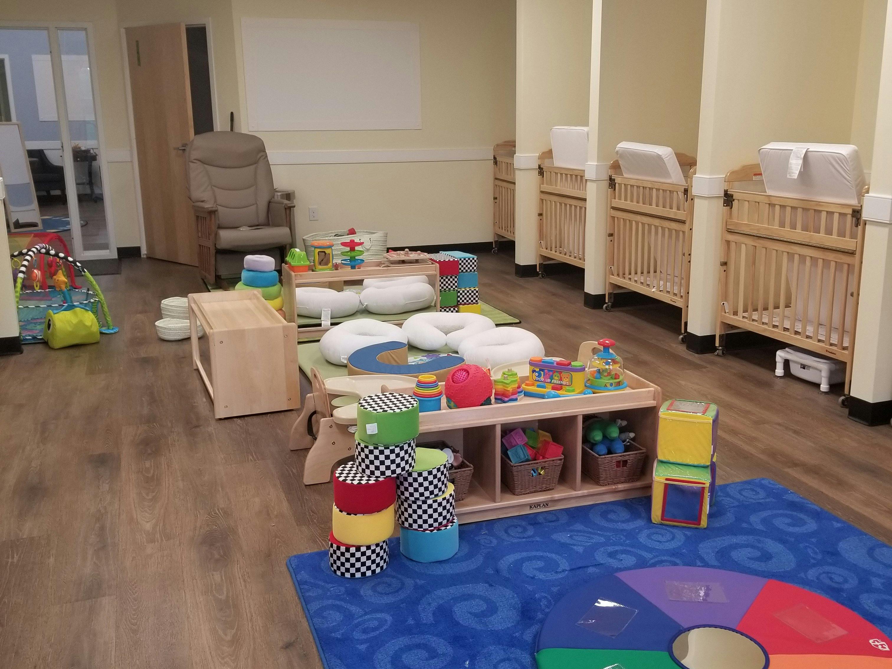 A classroom with several cribs, child-friendly toys, and cushions