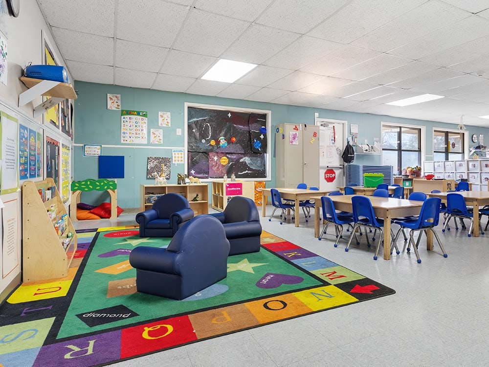 Colorful classroom with small tables and chairs, a play rug, and reading nook