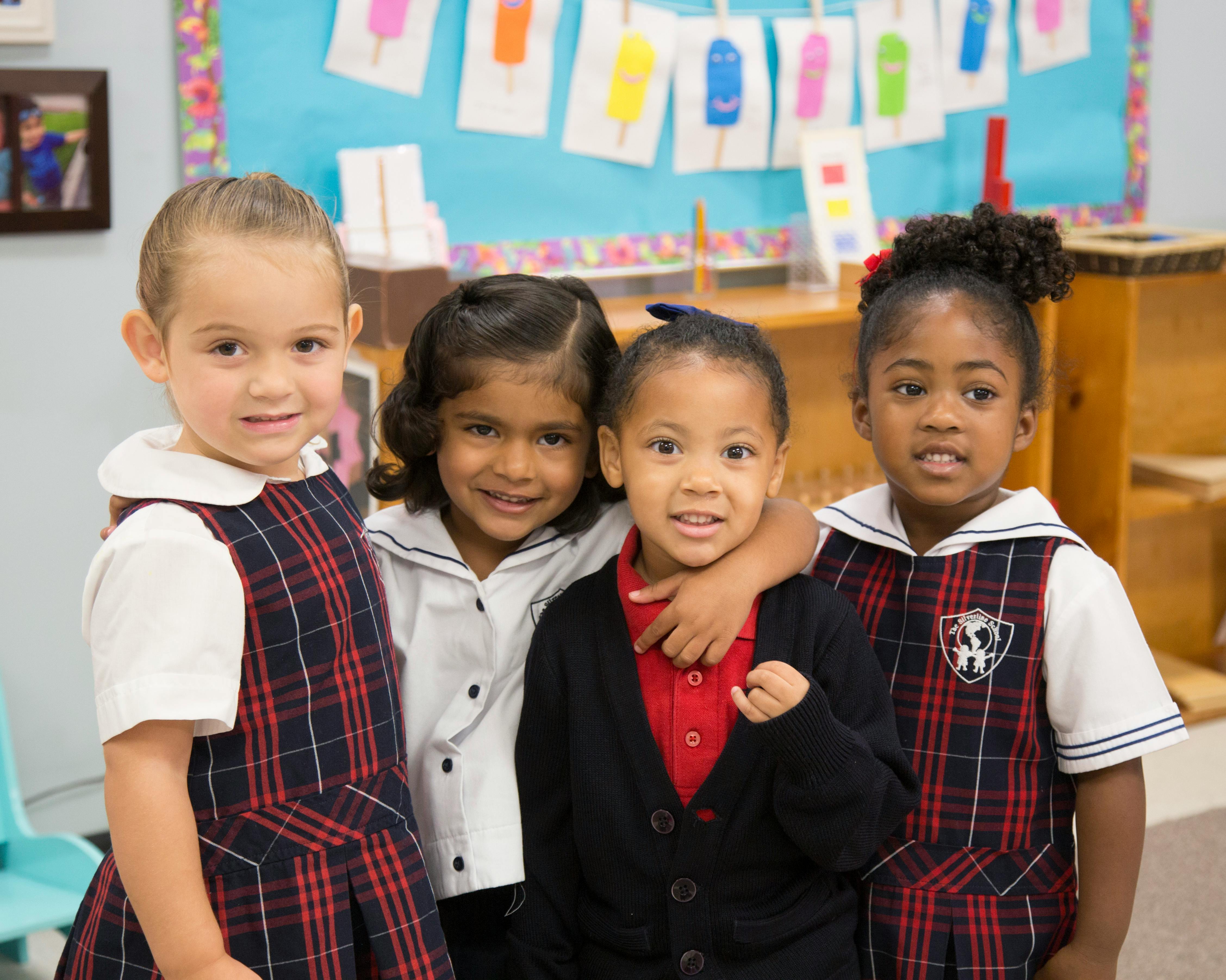 Four children in school uniforms standing together in a classroom