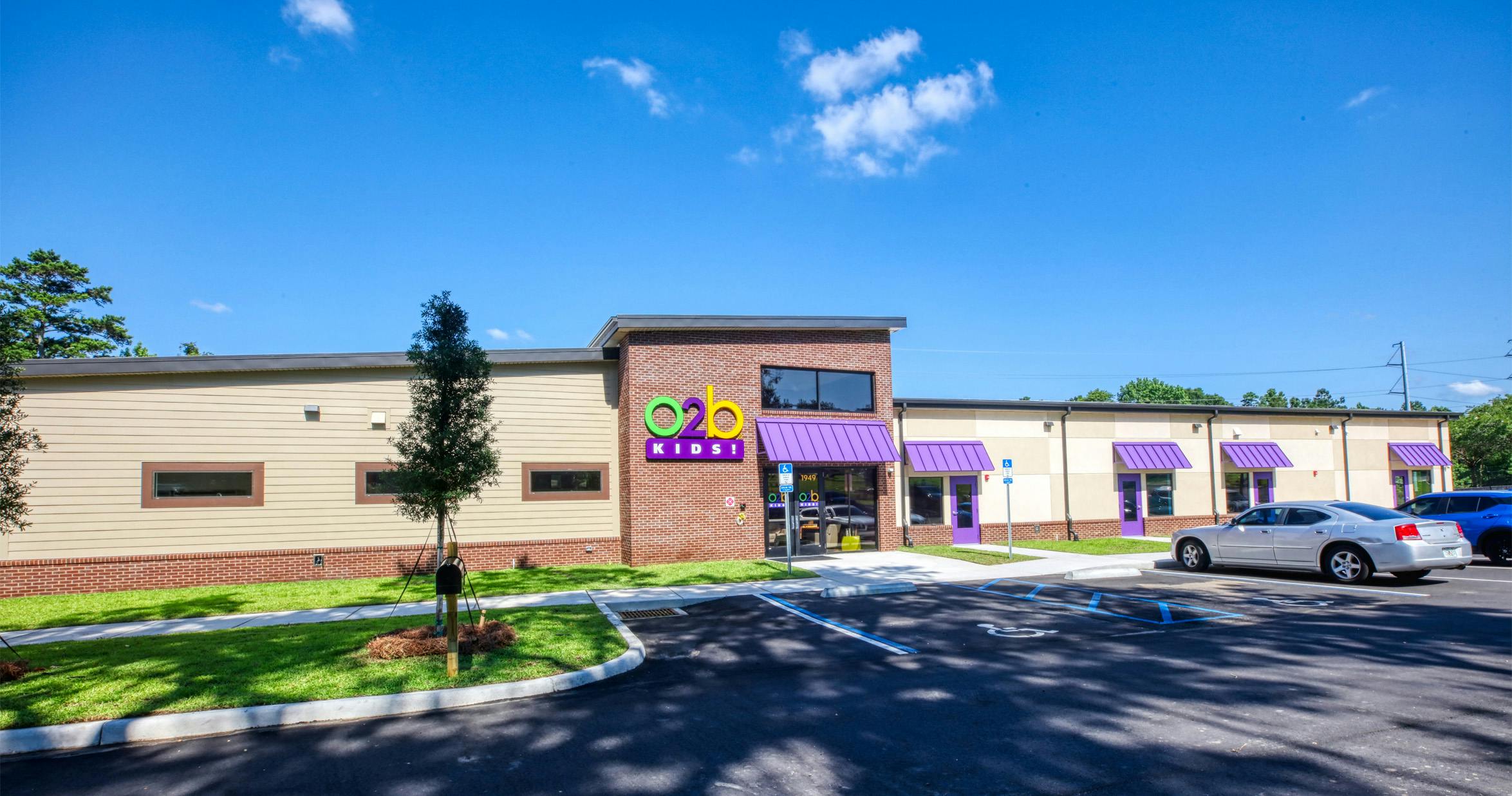 Exterior view of an O2B Kids! facility with a brick and tan facade, purple awnings