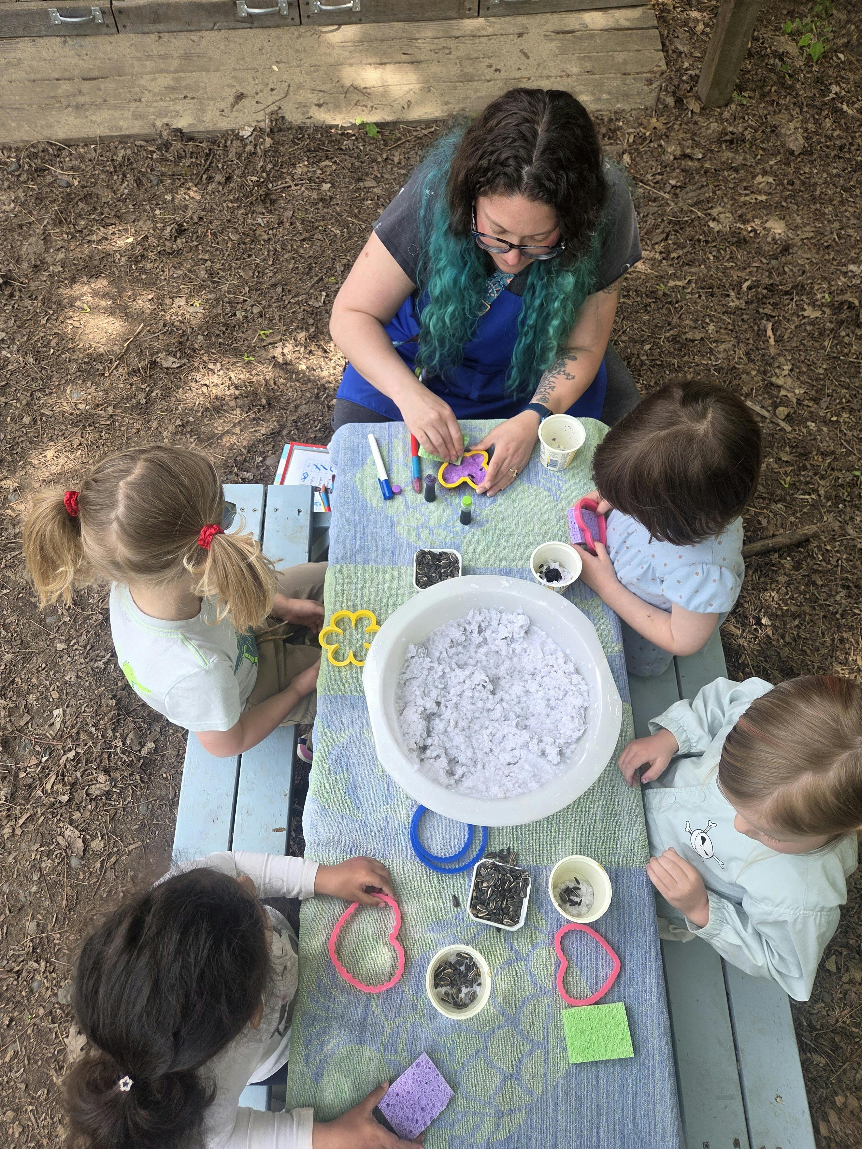 Adult and children at a table with craft supplies and a large bowl of white material