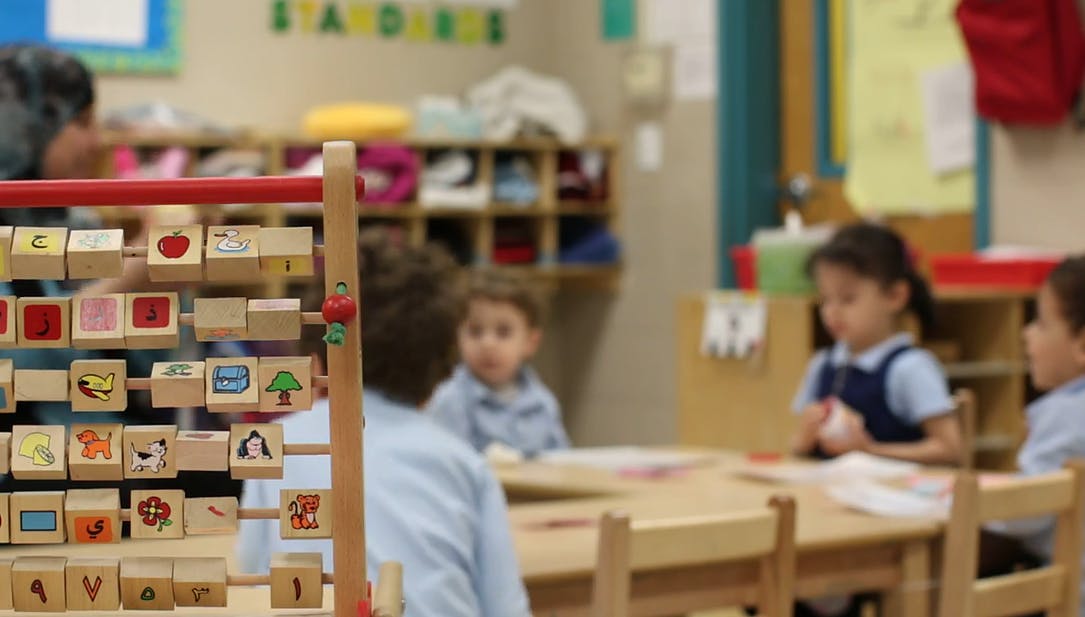 Children sitting at a table in a classroom with an abacus in the foreground