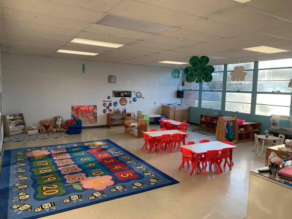 Empty classroom with small red tables and chairs, and a large number rug