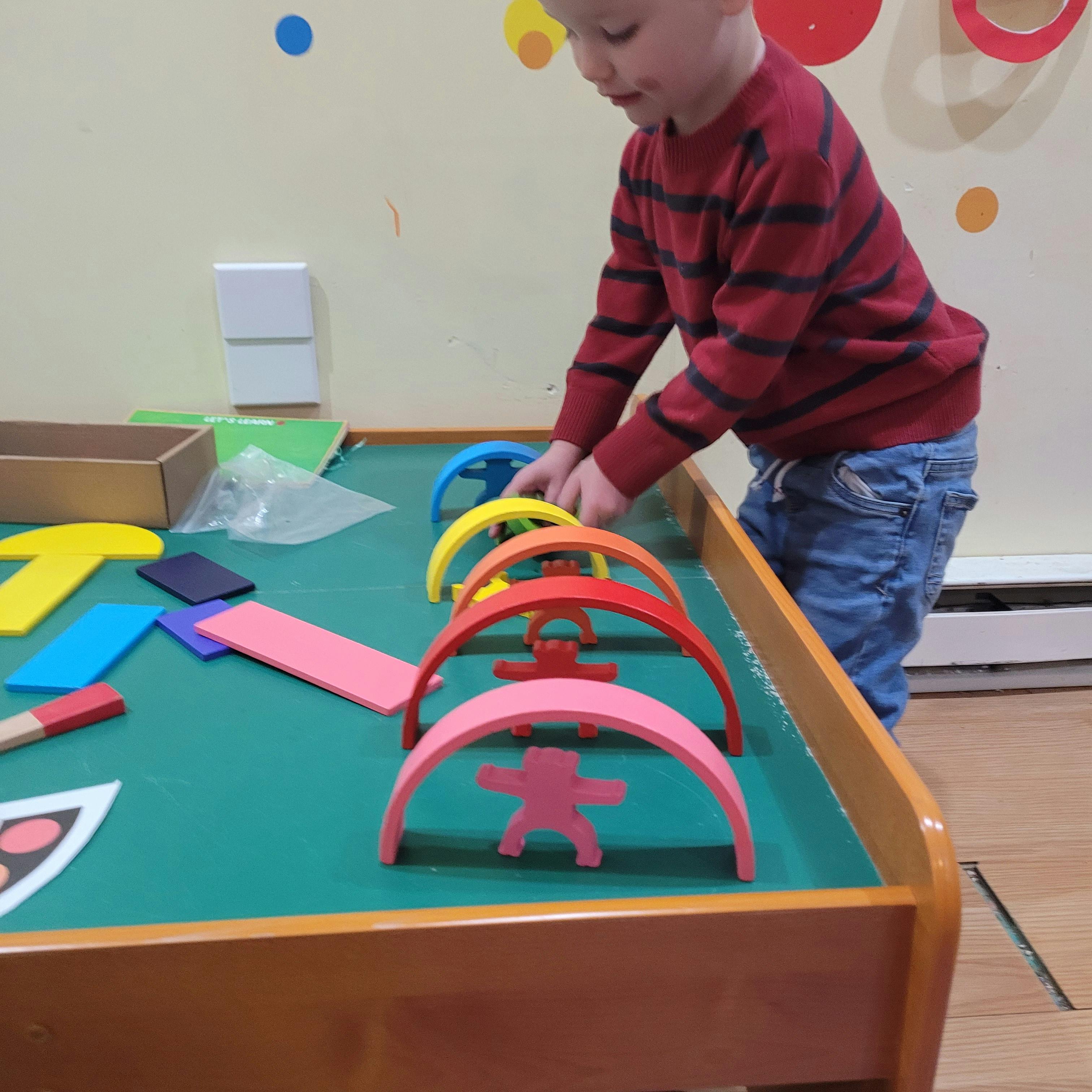 Child playing with colorful arch-shaped blocks on a green table