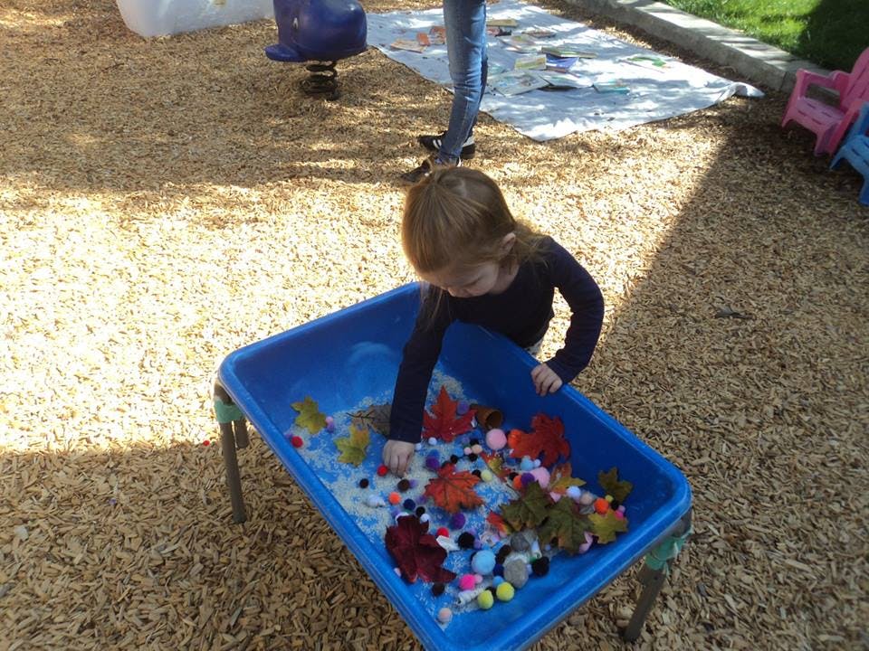 Child playing with colorful objects in a blue sensory bin