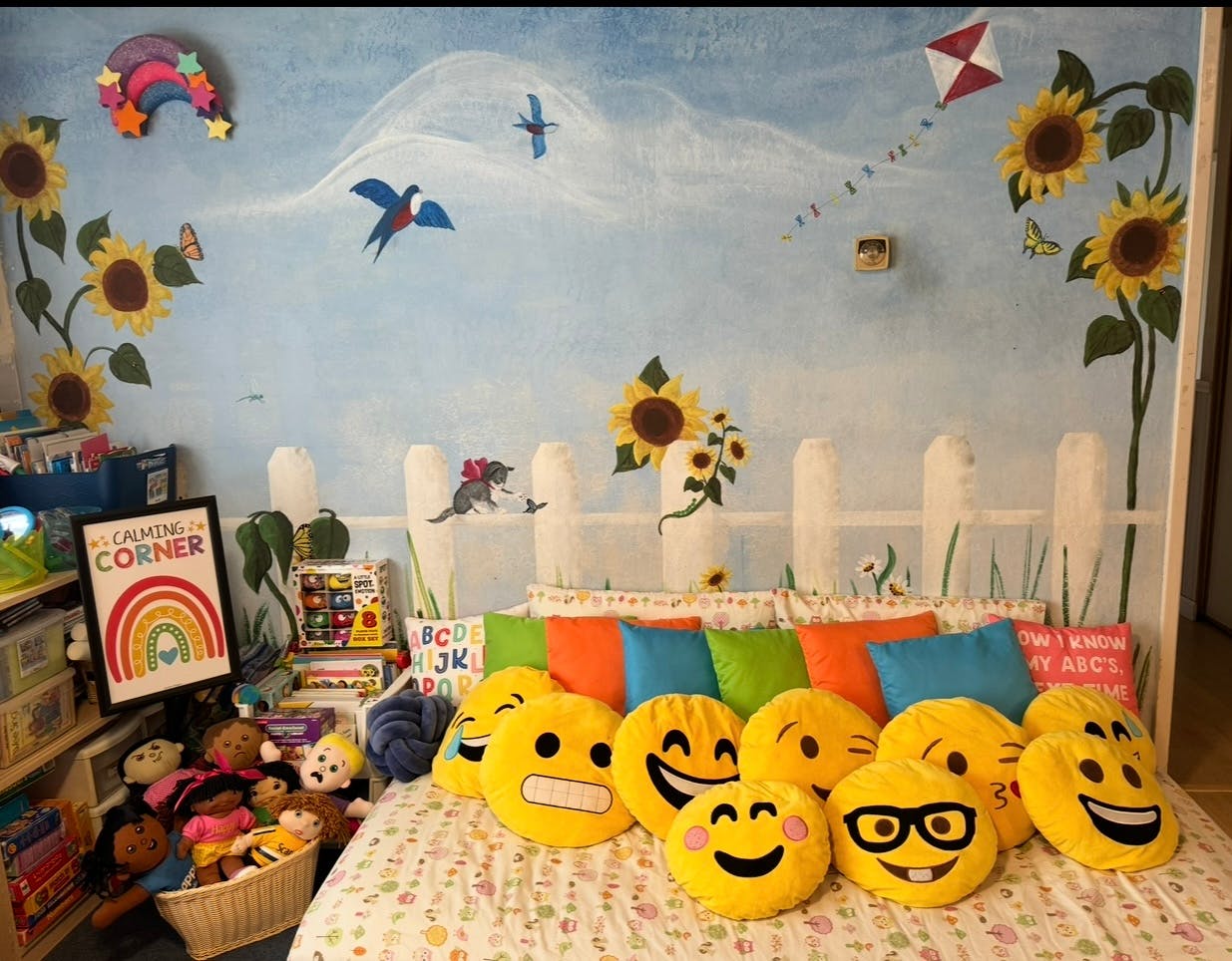 Bed with emoji pillows against a wall mural of sunflowers and birds