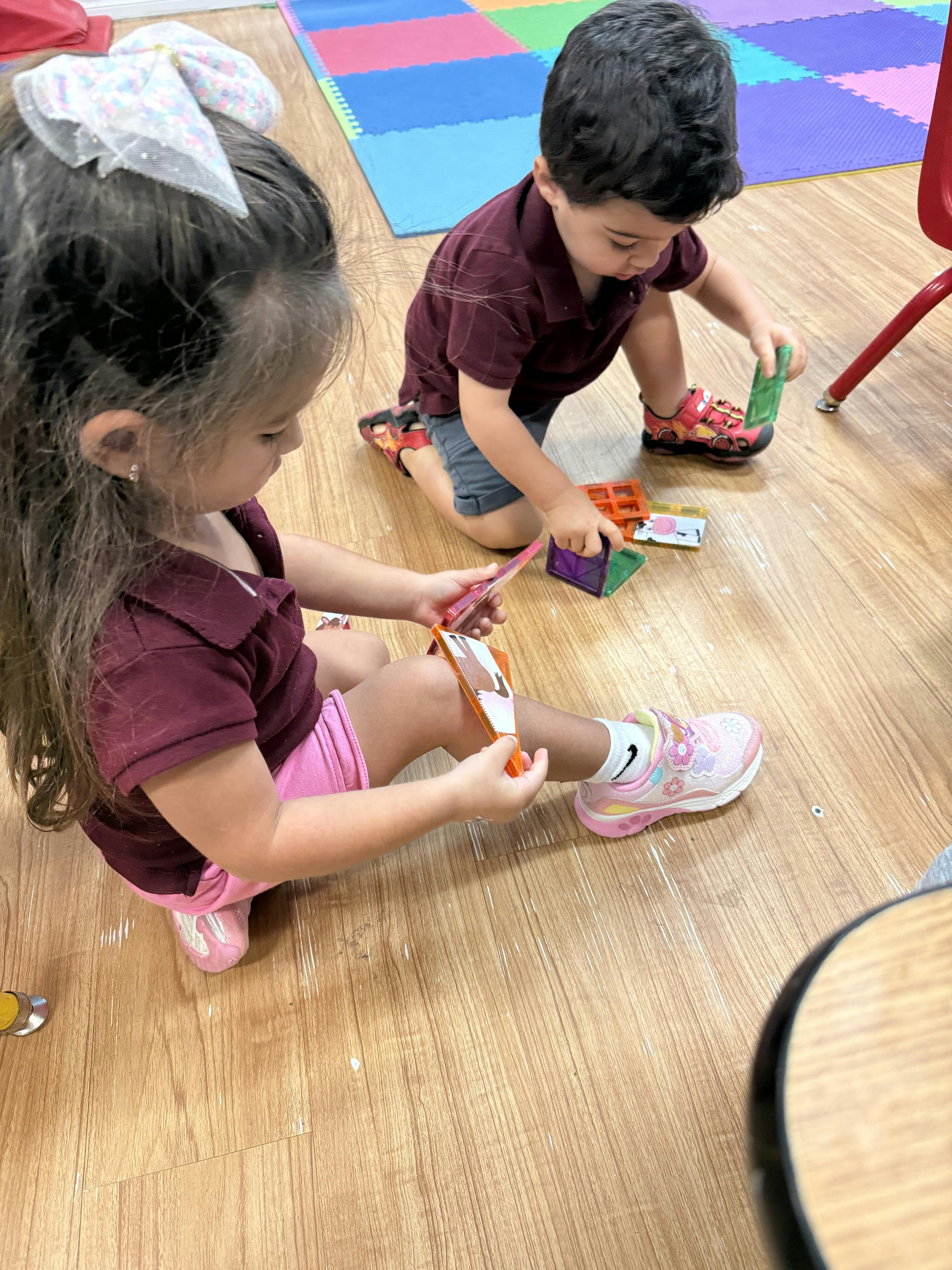 Two children playing with colorful magnetic tiles on a classroom floor