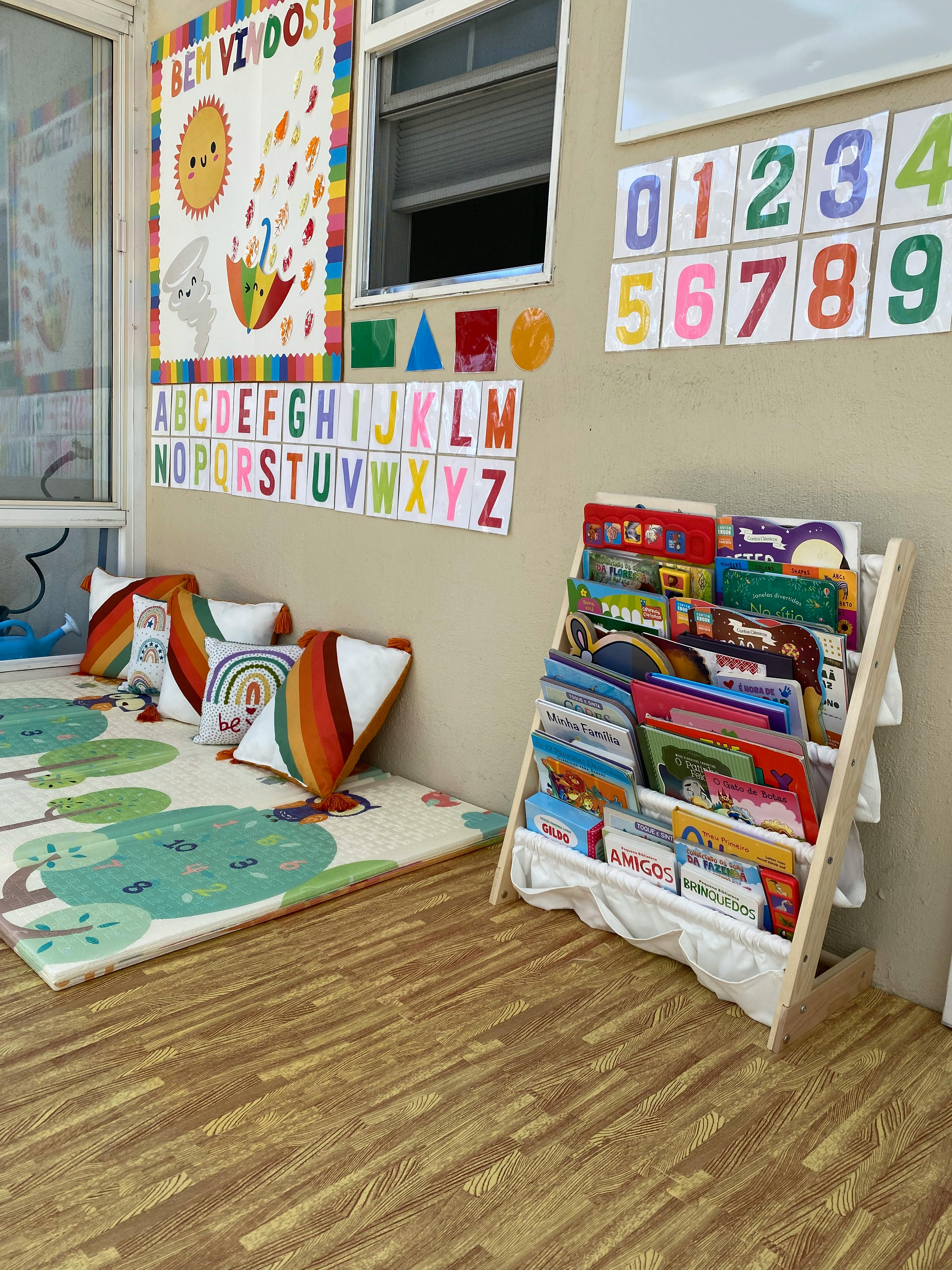 Children's play area with a rug, pillows, a bookshelf, and wall decorations