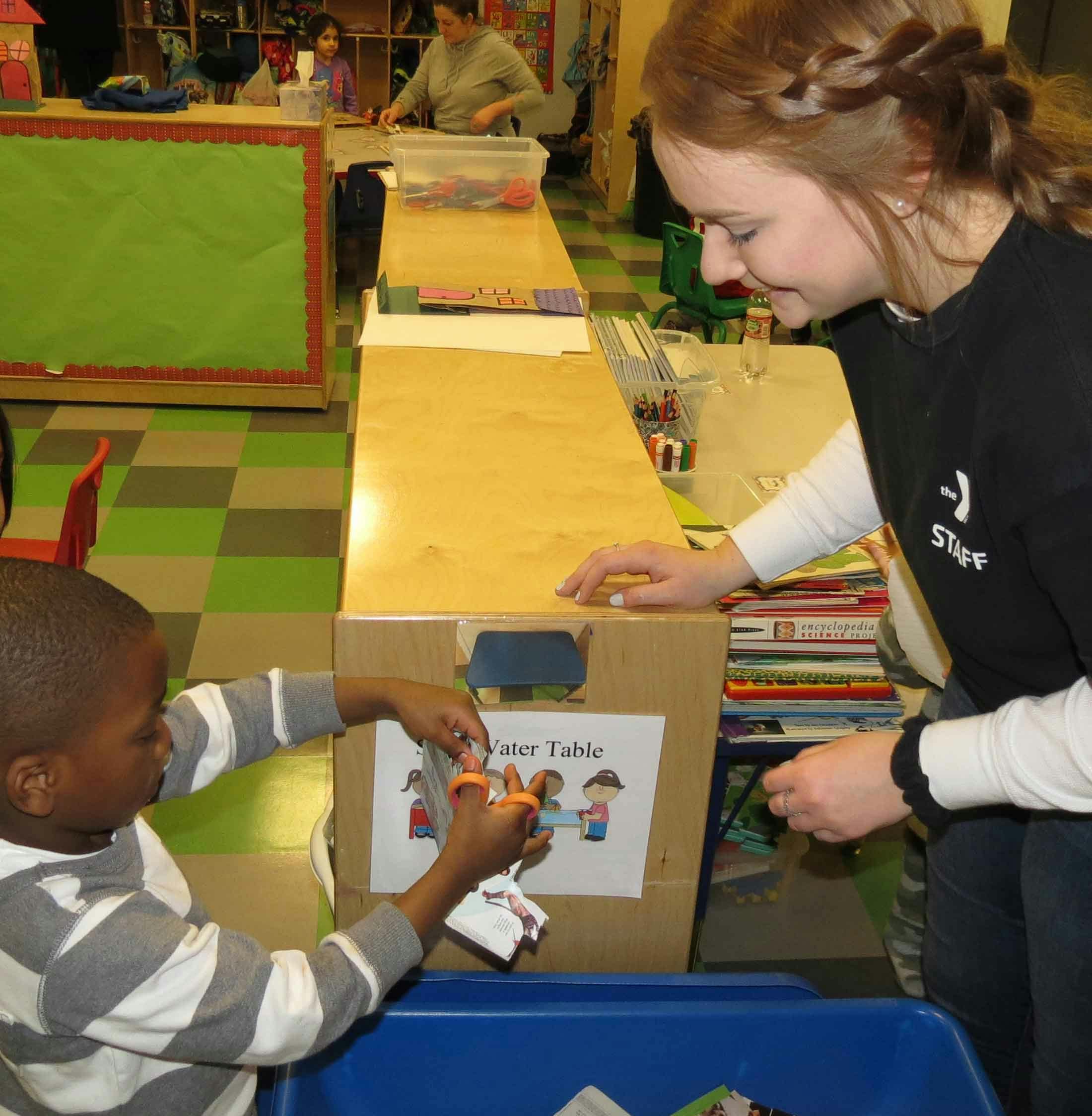 Adult and child cutting paper with scissors in a classroom