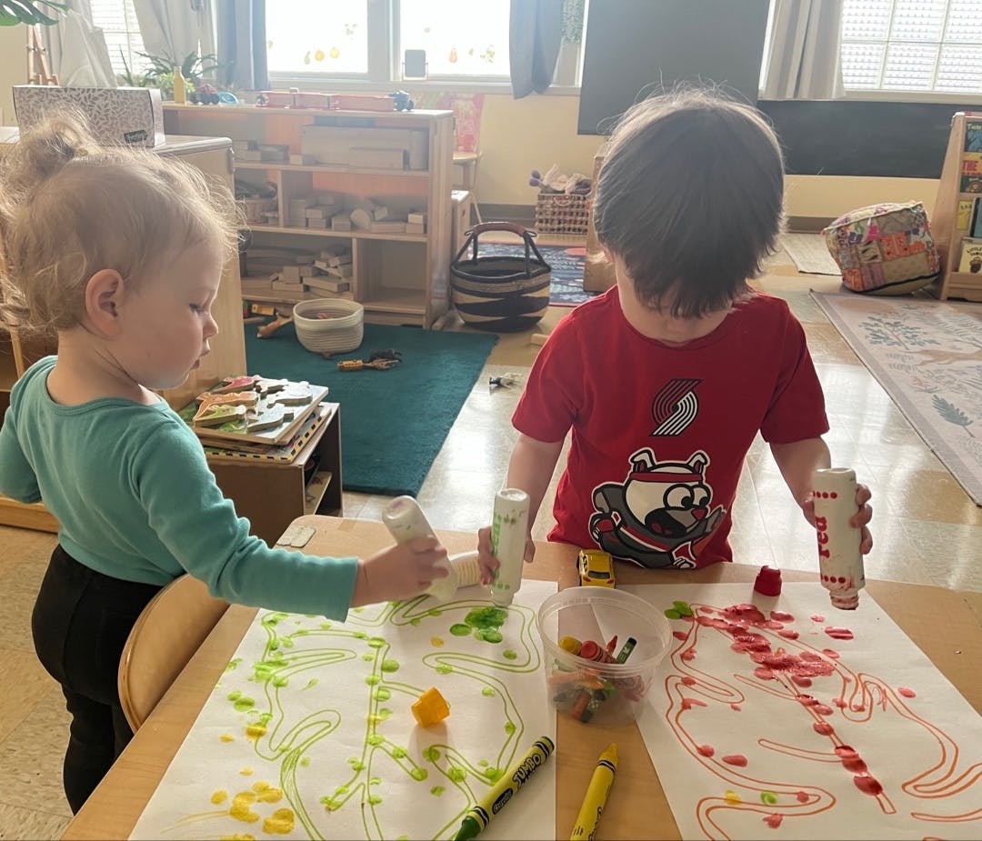 Two children creating art with squeeze bottles and paper in a classroom
