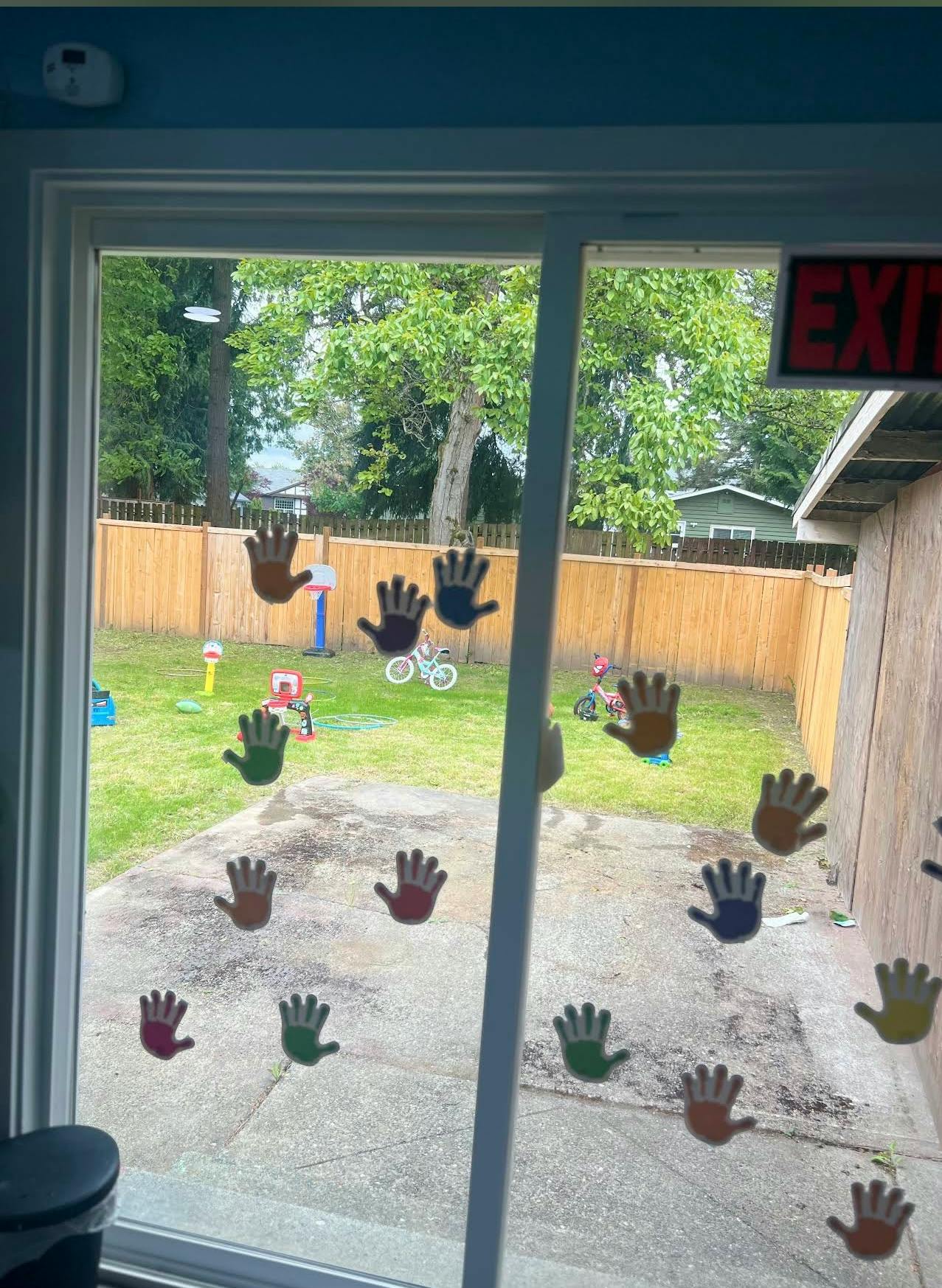 Window with handprint cutouts looking out to a backyard with play equipment
