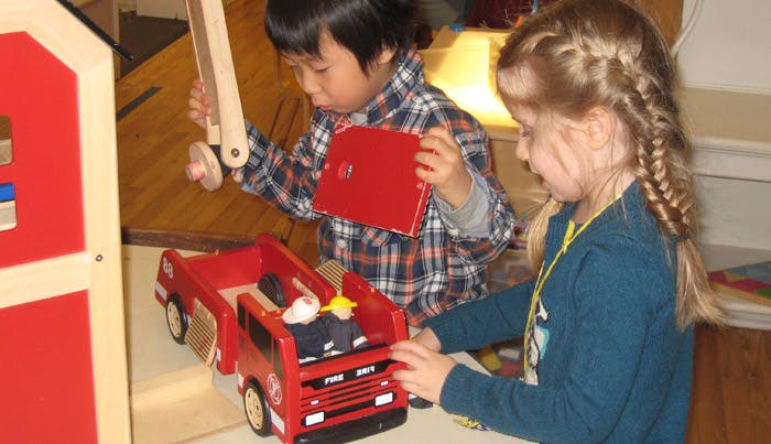 Two children playing with a red toy fire truck