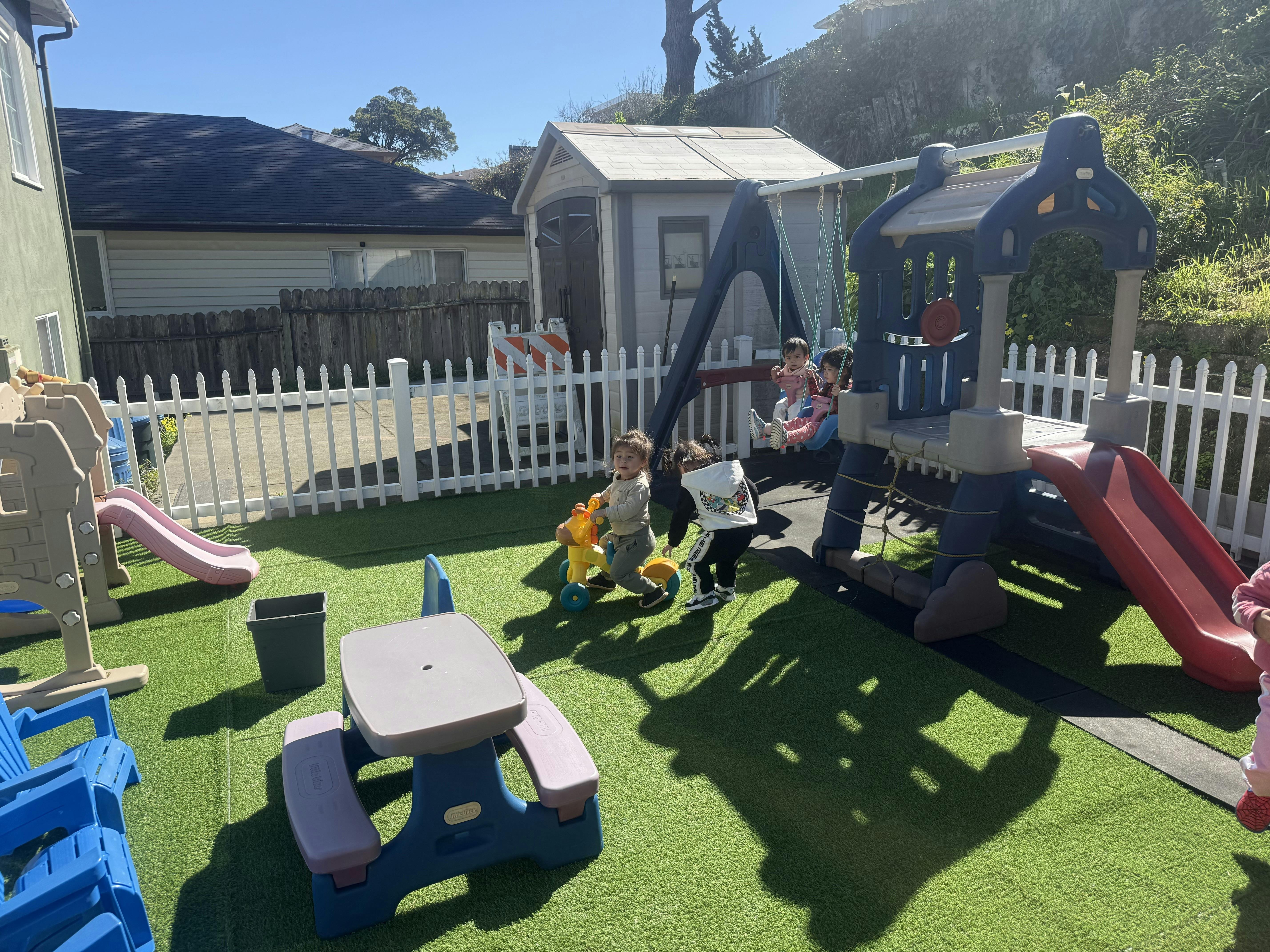 Children playing on a swing set and toy ride-on in a backyard
