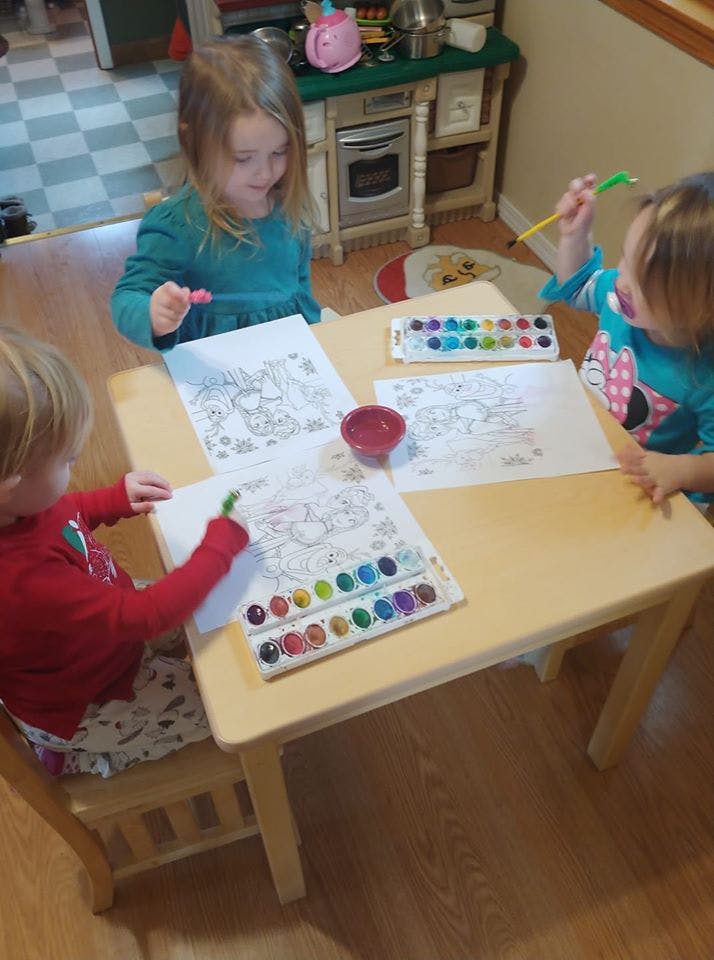 Three children painting at a table with watercolors at a small table