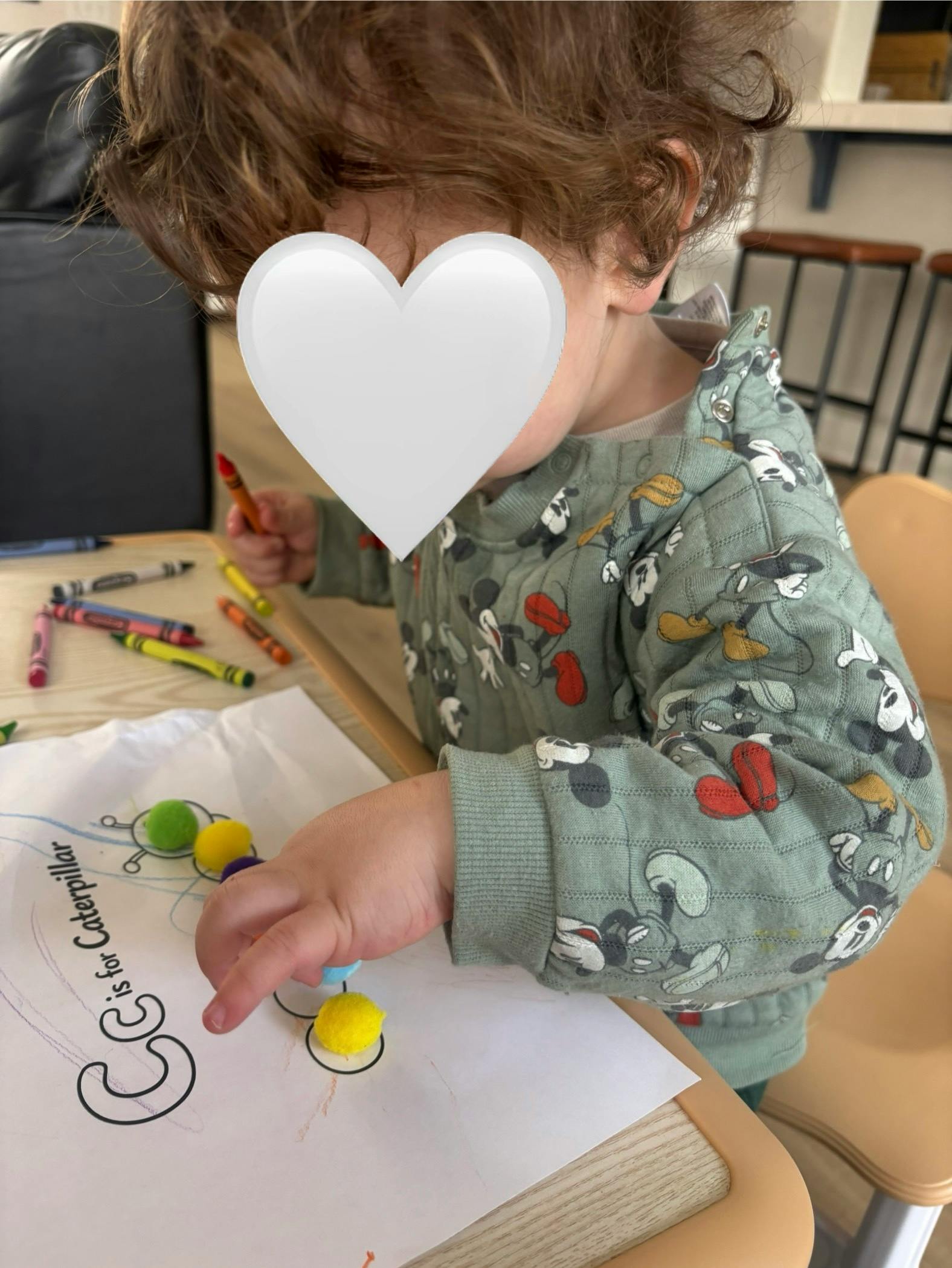 child coloring and playing with pom-poms on a paper with "C is for Caterpillar"