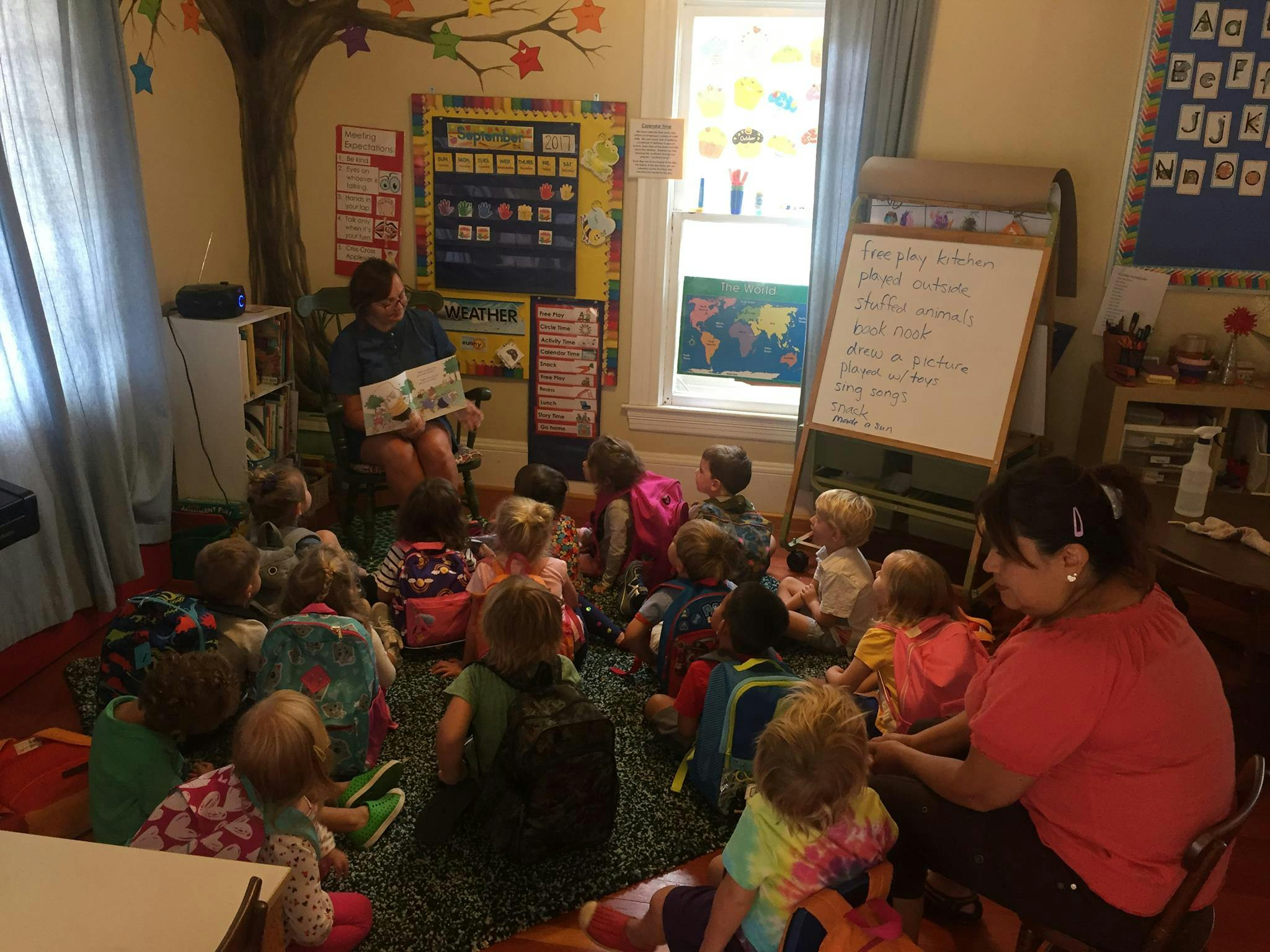 Adult reading a book to a group of children in a classroom