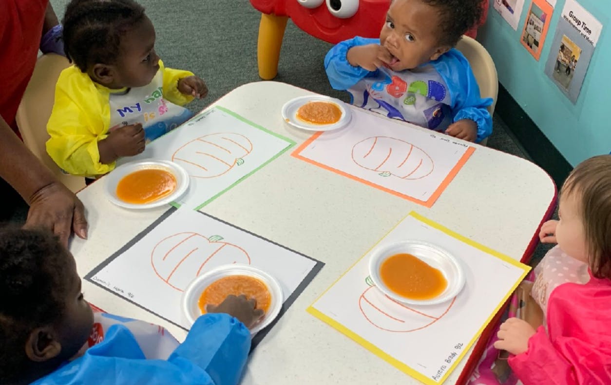 Children at a table with pumpkin drawings and orange paint