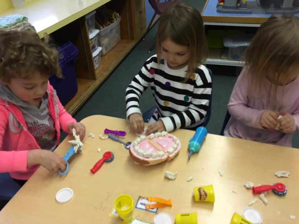 Three children playing with a dental model and playdough at a table