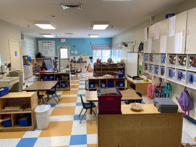 Classroom with tables and chairs, shelves, a sink, and a teacher board