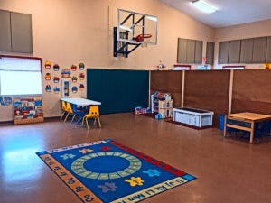 Indoor play area with a basketball hoop, tables, and a colorful rug