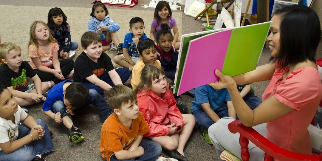 Person reading a large book to a group of children in a classroom