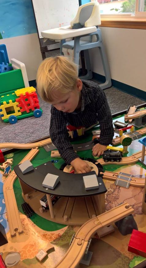 Child playing with a wooden train set on the floor