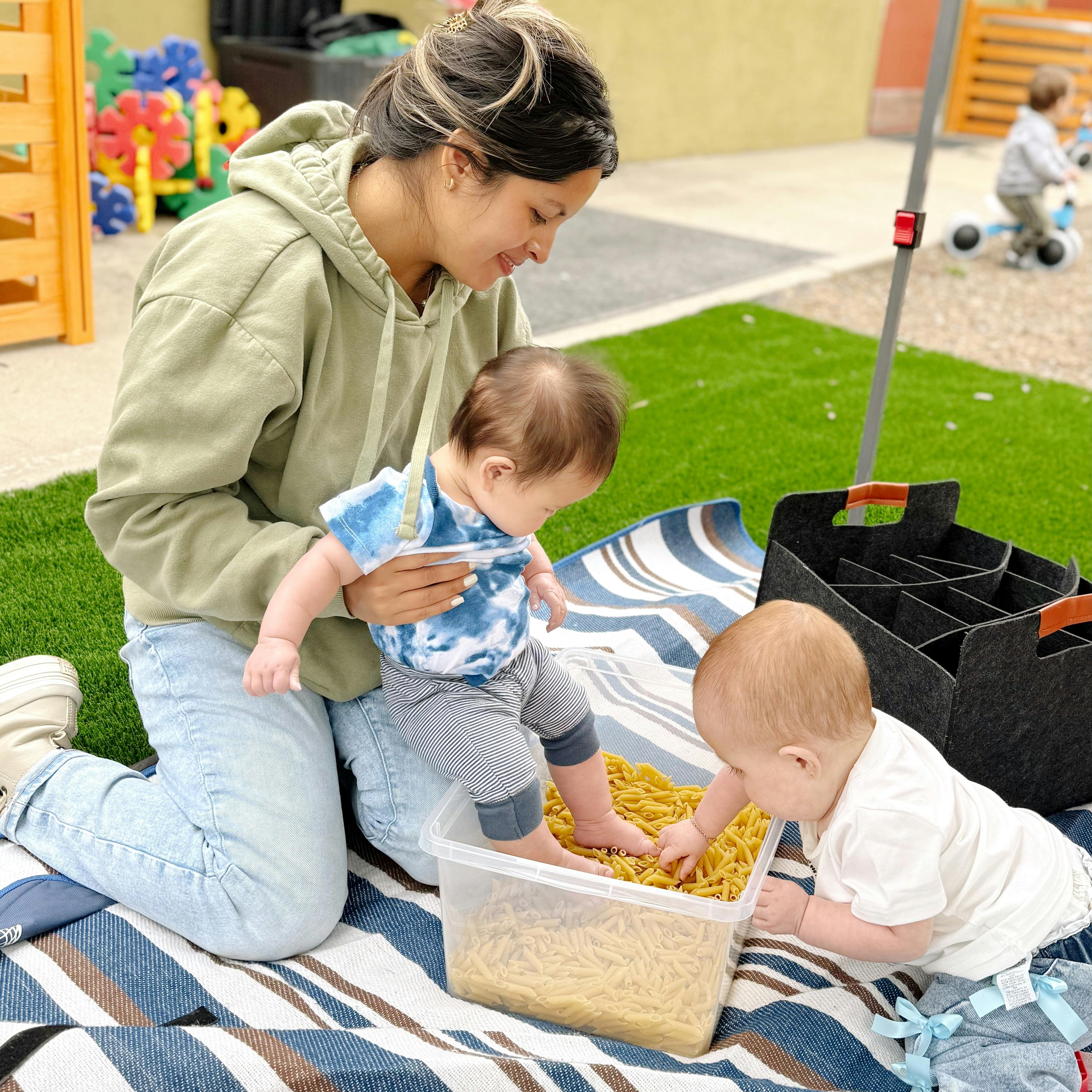 Person holding a child with foot in a bin of pasta, another child reaching into it