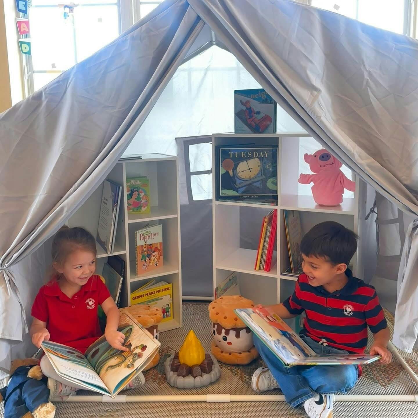 Two children reading books inside a blanket fort