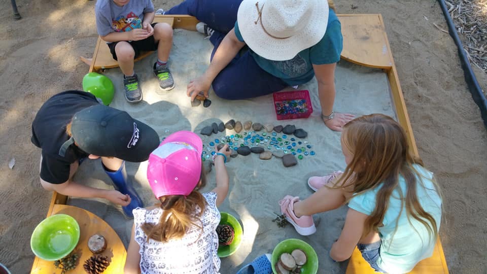 Adults and children playing with natural materials in a sandbox