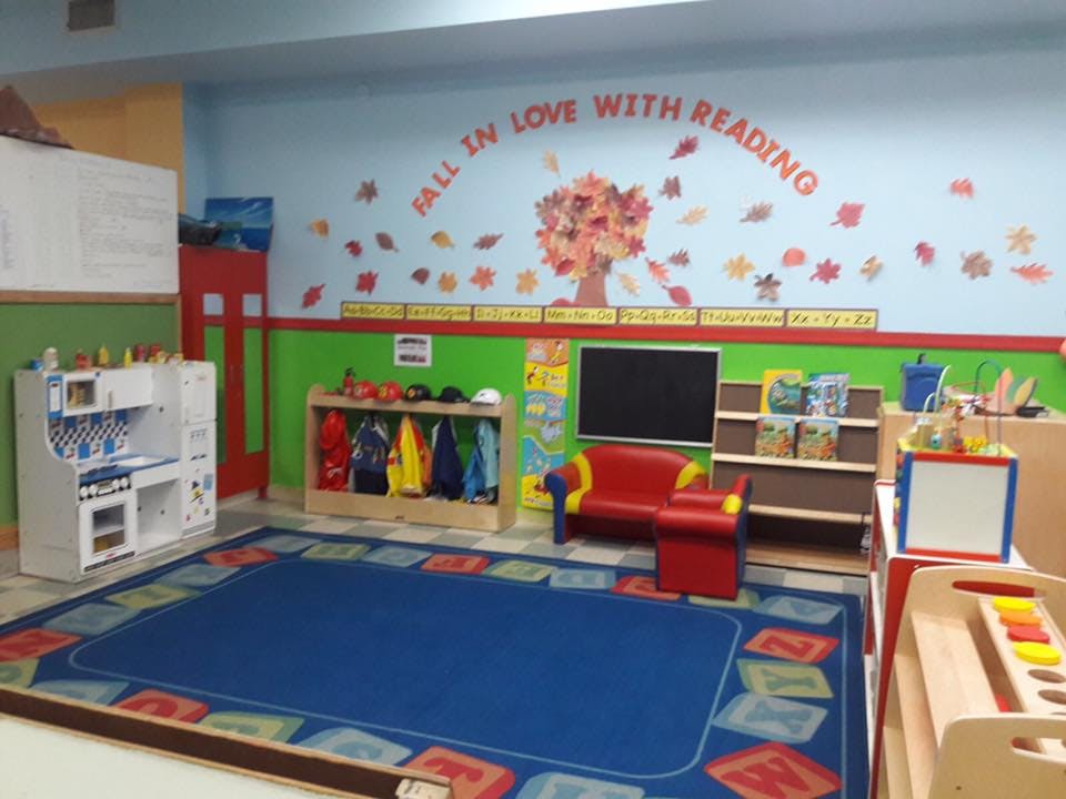 Classroom with blue rug, play kitchen, coat rack, and reading nook