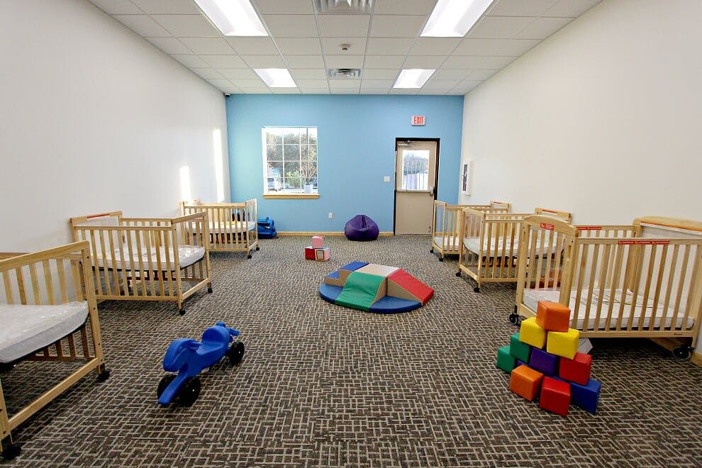 Room with multiple cribs, toys, and a blue wall