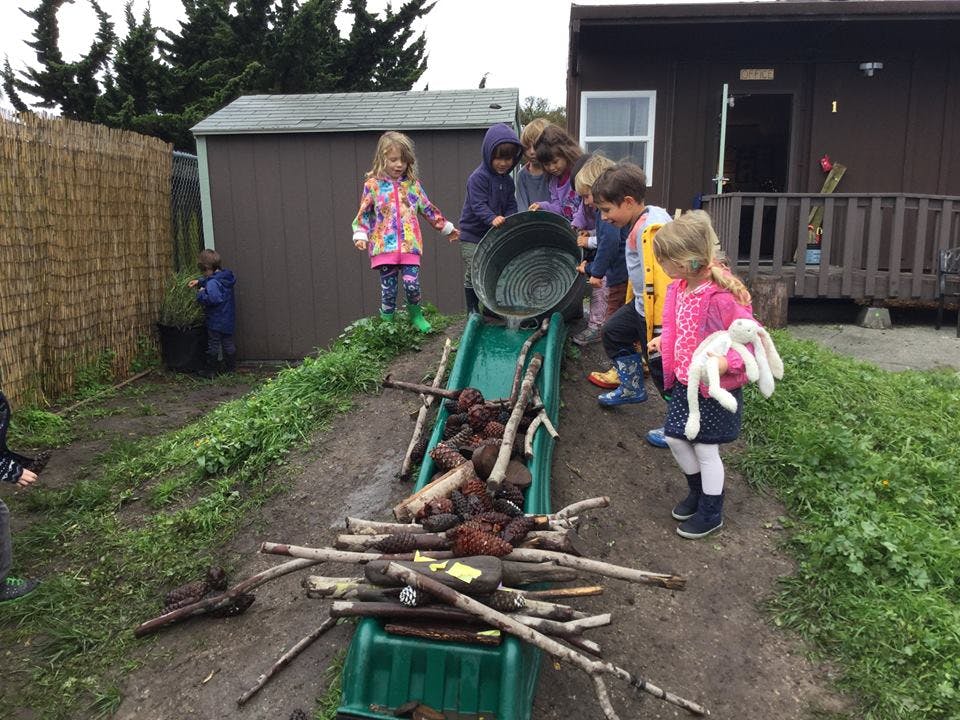 Children playing with a bucket and sticks on a slide outdoors