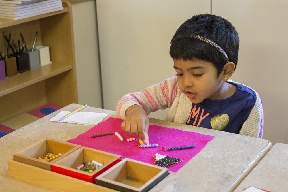 Child sorting small objects on a pink mat at a table