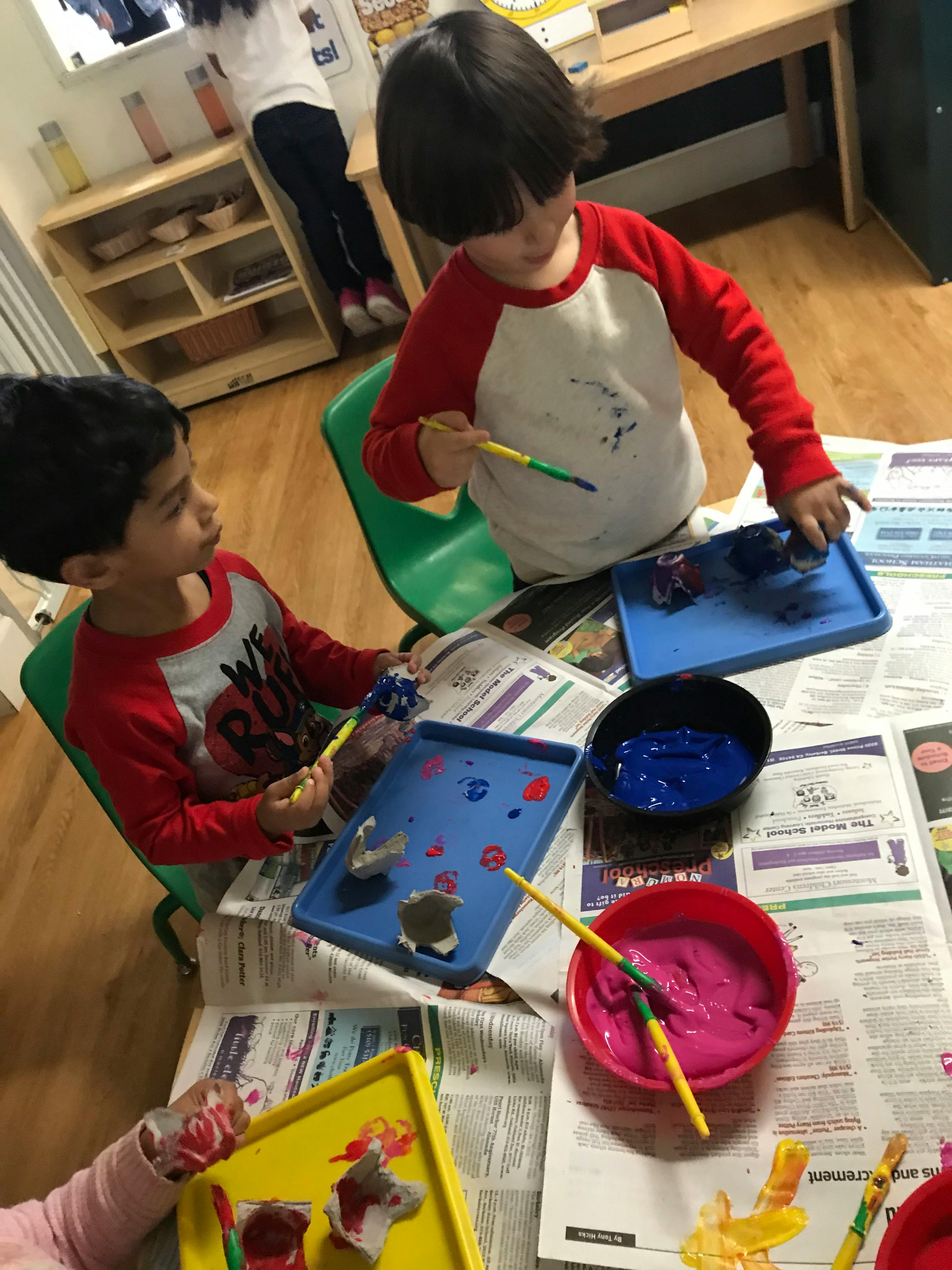 Two children painting at a table covered with newspaper