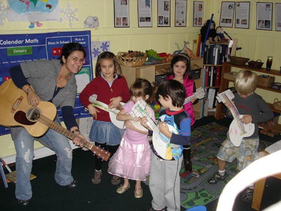 Person playing guitar with children holding toy guitars in a classroom