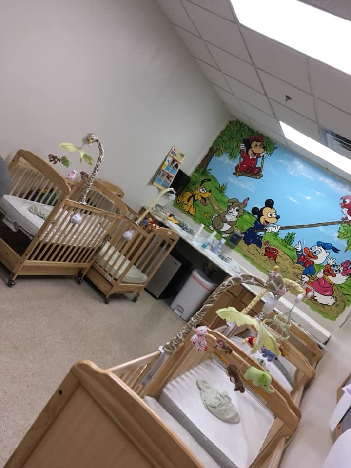 Nursery room with multiple wooden cribs and a cartoon mural on the wall