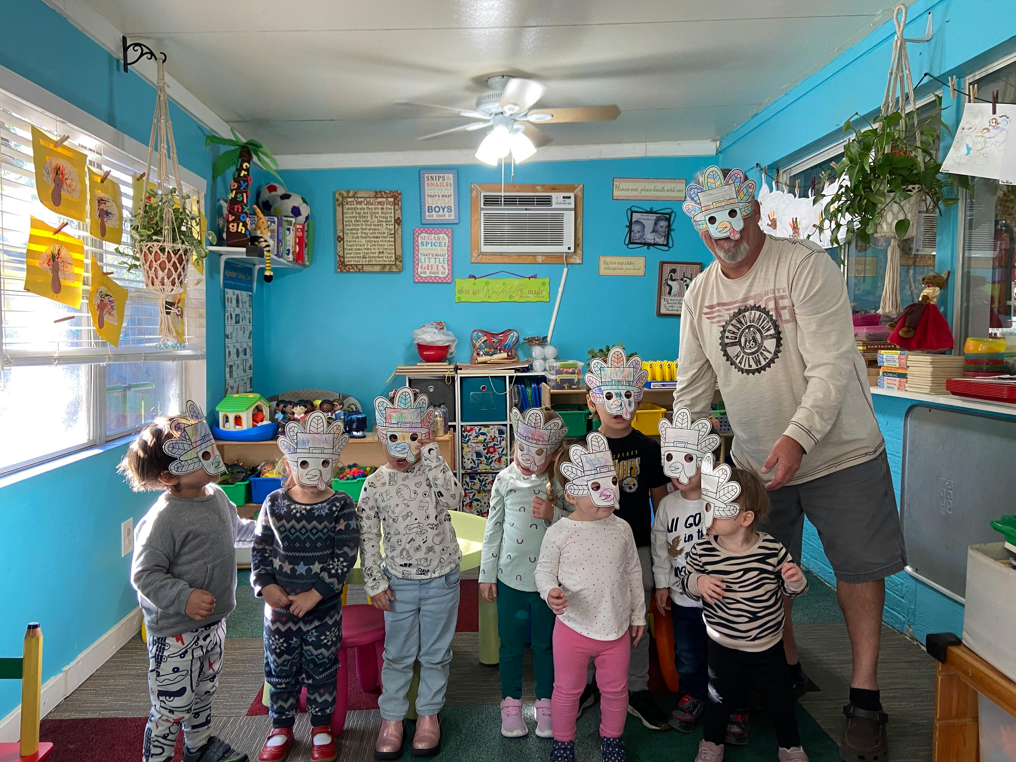 Group of children and one adult wearing paper turkey masks in a playroom