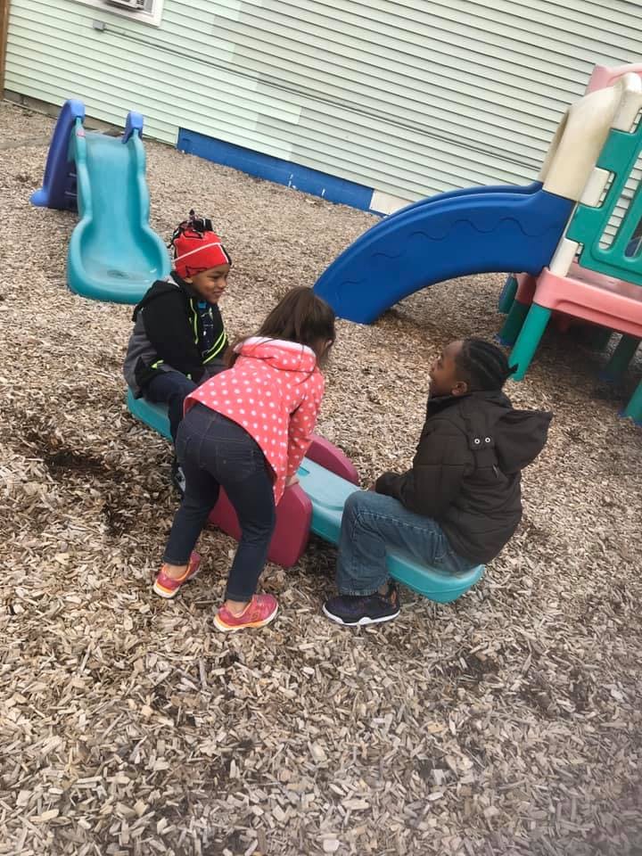 Three children playing on a seesaw in a playground
