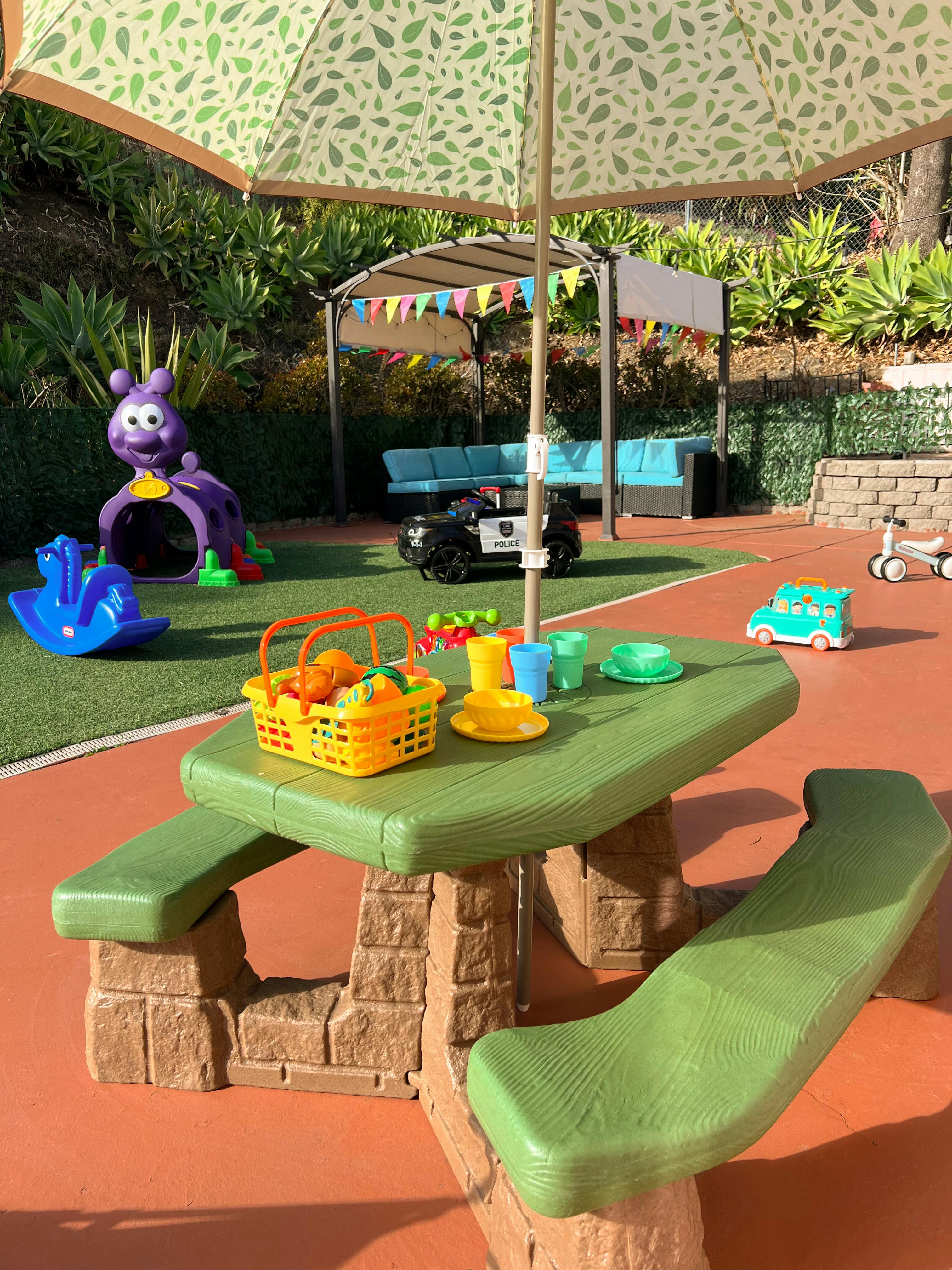 Children's picnic table with toy food and dishes under an umbrella
