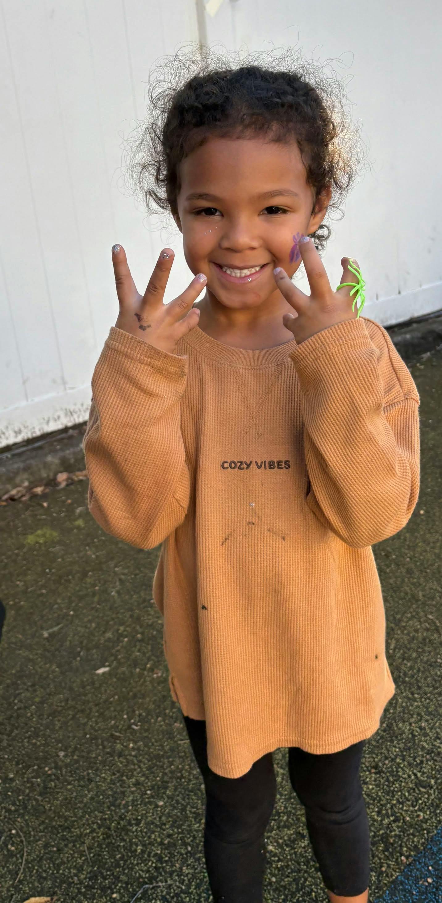 Child smiling while holding up hands with face paint and a toy spider